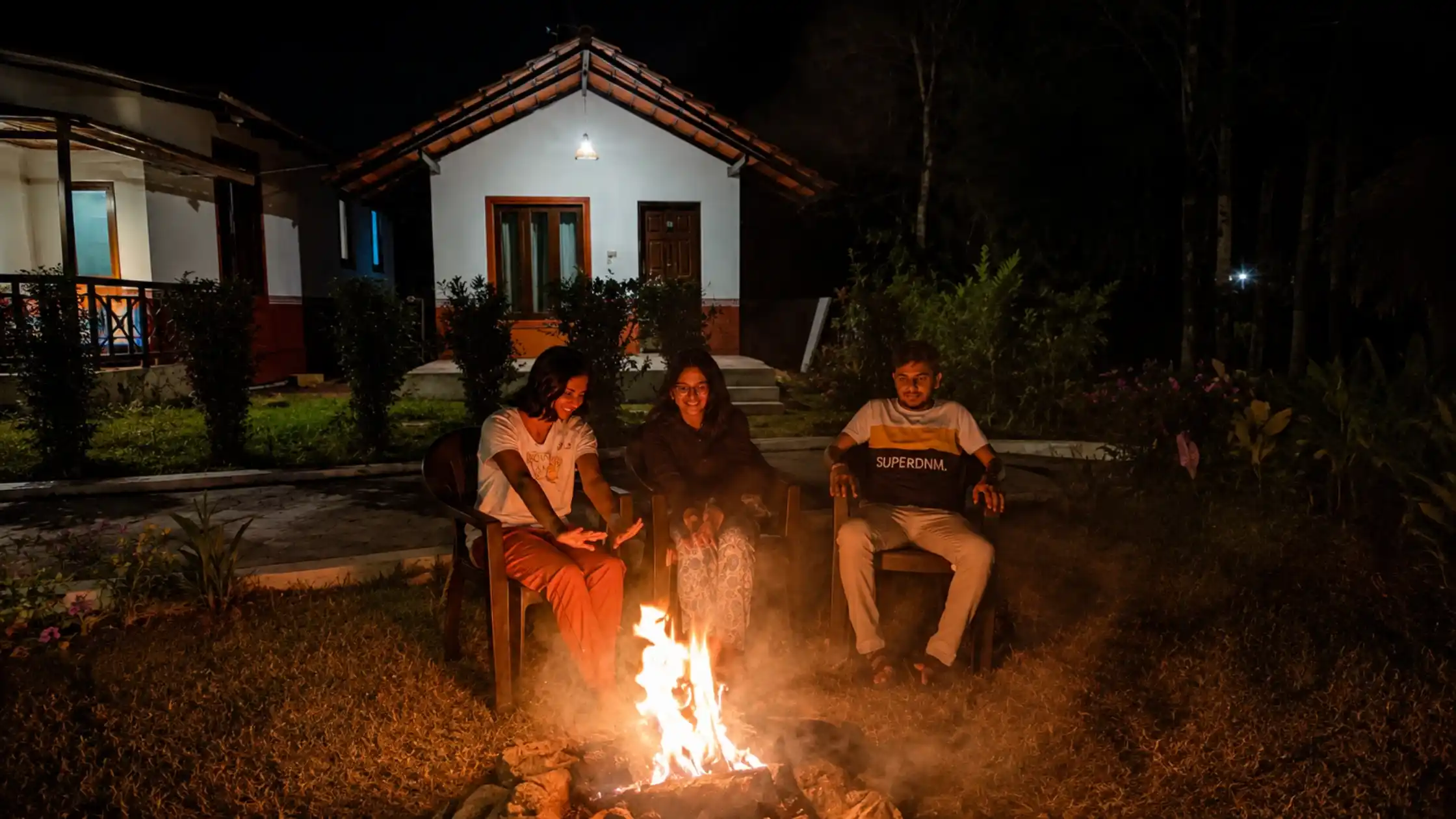 Guests enjoying a campfire at a day outing resort in Sakleshpur, surrounded by cottages and greenery at night